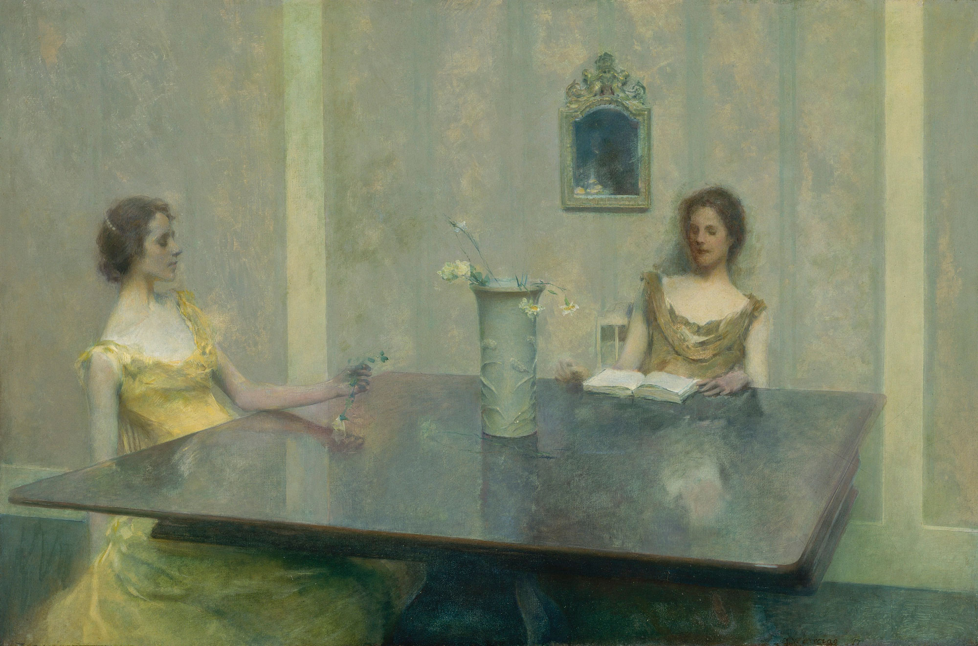 Two women wearing formal dresses sit at a large table, one reads a book. There is a vase of flowers at the center of the table.