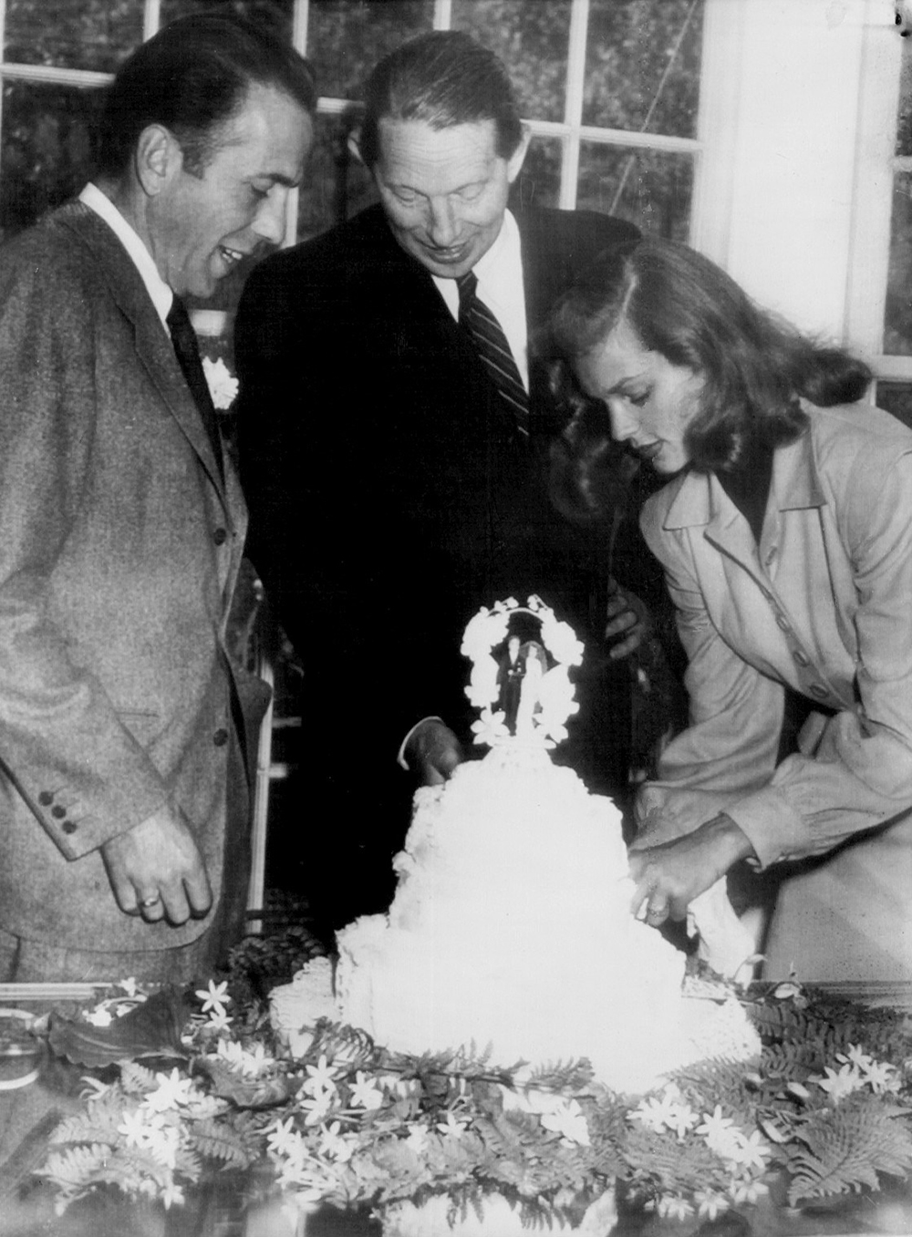 Grouped around their wedding cake are Humphrey Bogart (left), Louis Bromfield, best man, and Lauren Bacall, the bride, 1945. Photograph by the Tucson Daily Citizen. Wikimedia Commons.