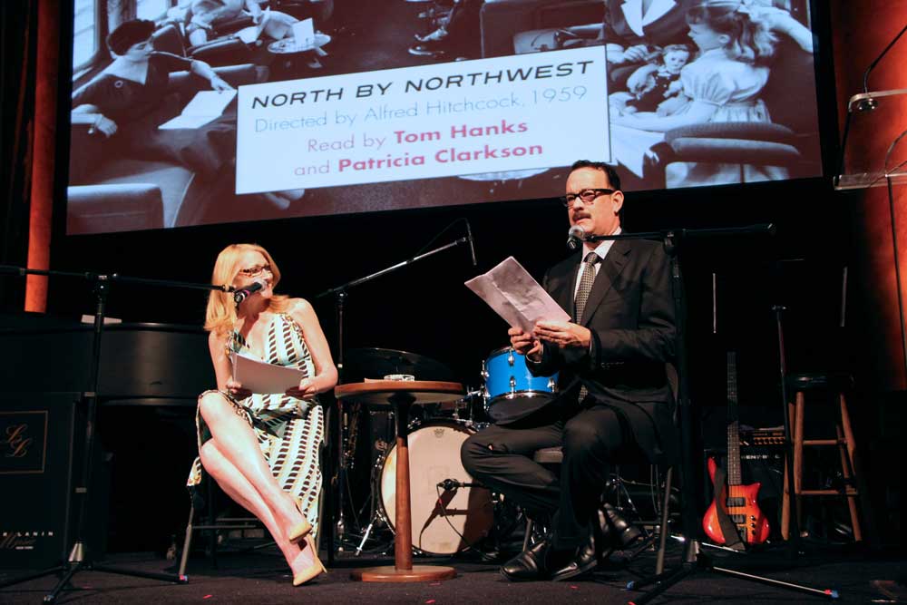 A woman and man onstage reading in front of an image from North by Northwest