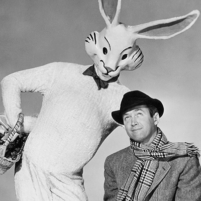 A giant white rabbit standing next to a man wearing a hat and scarf