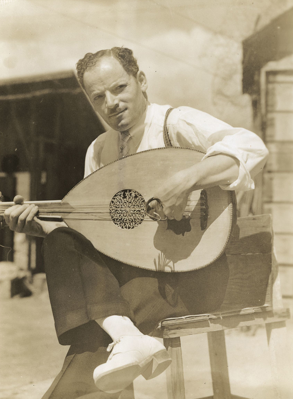A seated man plays an oud outdoors.
