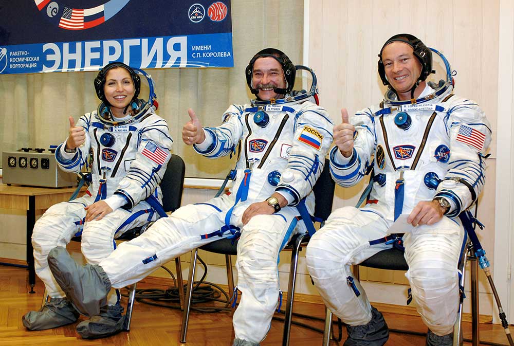 Anousheh Ansari, Mikhail Tyurin, and Michael E. López-Alegría before the Soyuz TMA-9 launch, Baikonur, Kazakhstan, 2006. Photograph by Bill Ingalls. Bridgeman Images. Three smiling astronauts in uniform seated while giving a thumbs-up