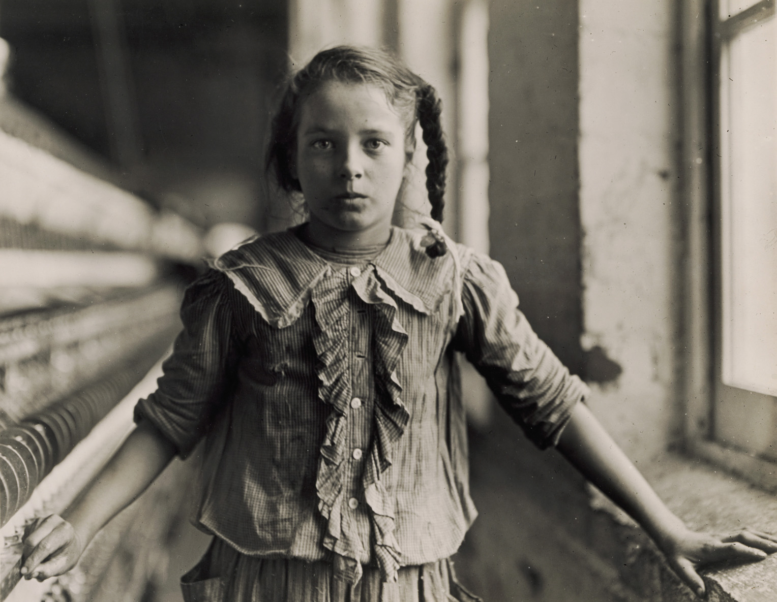 “Adolescent Girl, a Spinner, in a Carolina Cotton Mill” Back and white photograph of a young girl working in a factory in 1908.