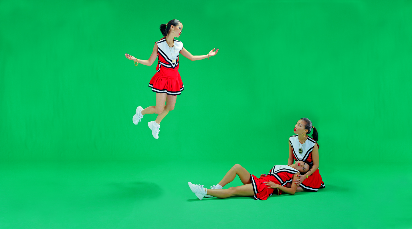 Color photograph of three cheerleaders against a green screen.