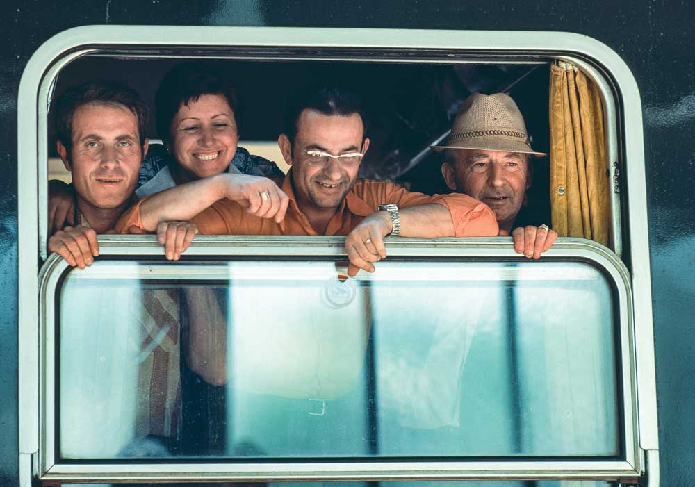 Four smiling people looking out the top of a train window.
