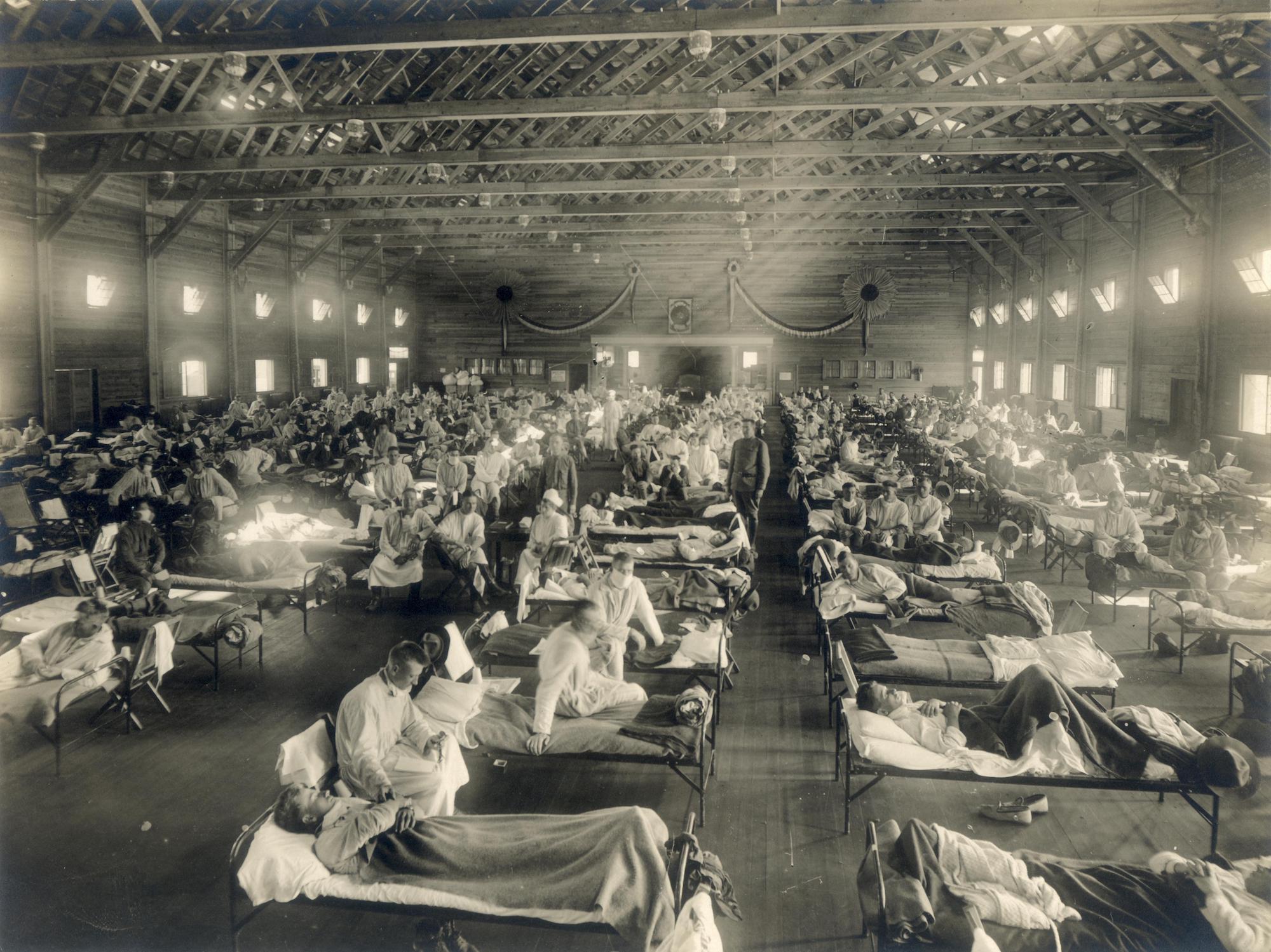 Emergency hospital during influenza epidemic, Camp Funston, Kansas, 1918. Otis Historical Archives, National Museum of Health and Medicine, New Contributed Photographs Collection. A black and white photograph showing beds with patients in an emergency hospital in Camp Funston, Kansas, in the midst of the 1918 influenza epidemic.