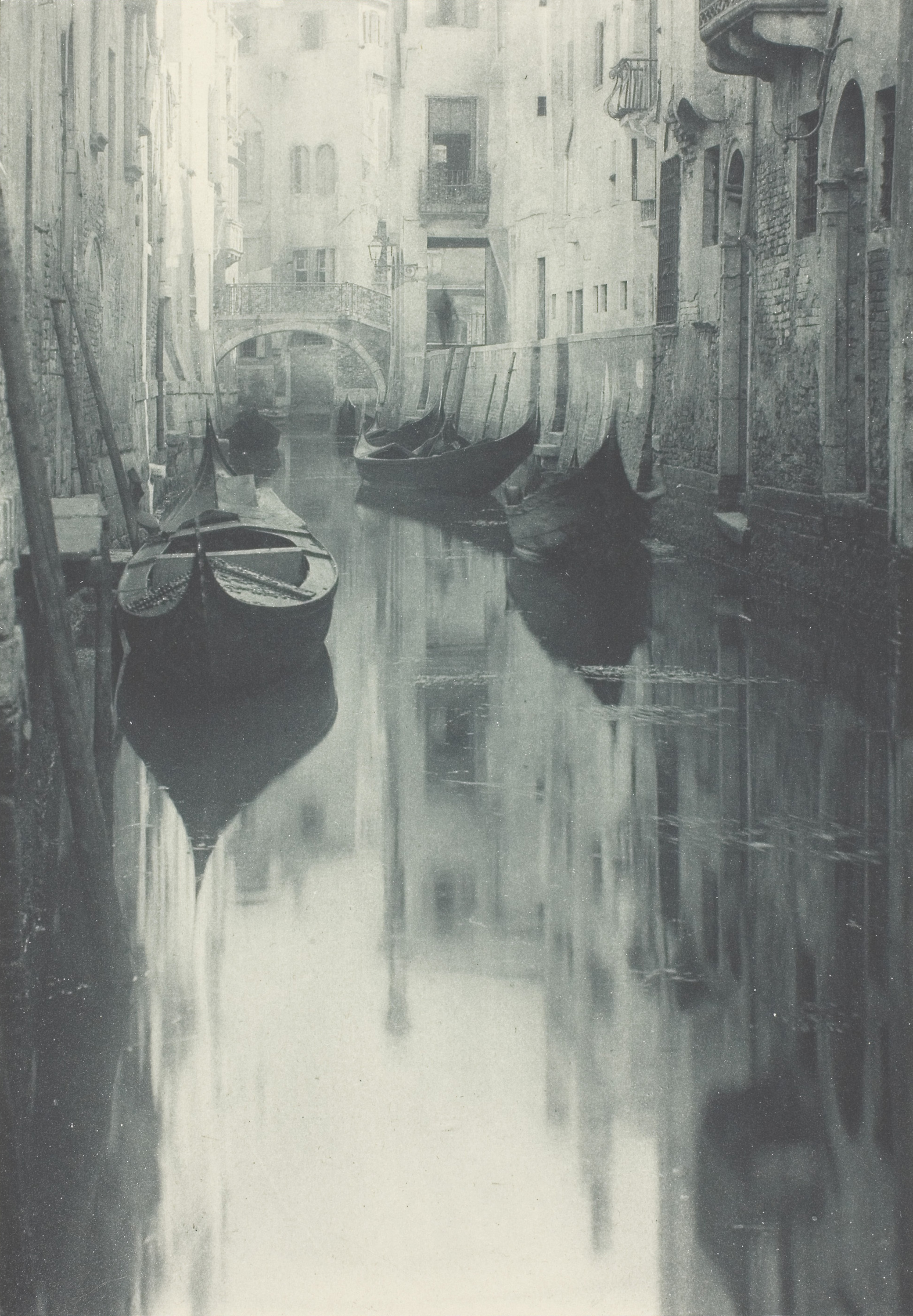 A photograph of empty boats on a Venice canal. In the canal you can see the reflection of the surrounding buildings and the boats.