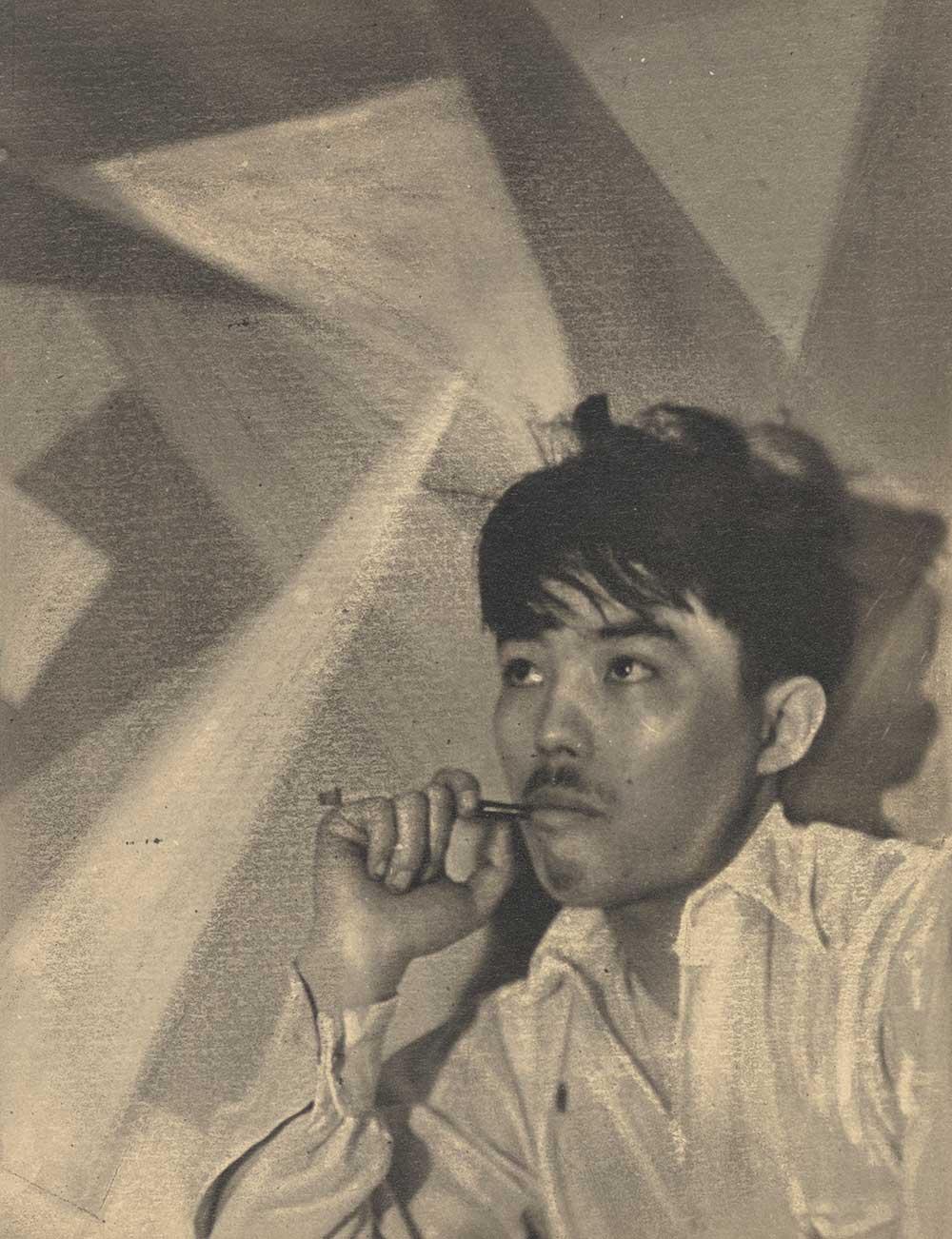 Photograph of a man with dark hair and a thin mustache smoking a cigarette in a holder. There is an abstract geometric background.