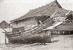 Sepia image of a curved wooden boat and a raised wooden building in water
