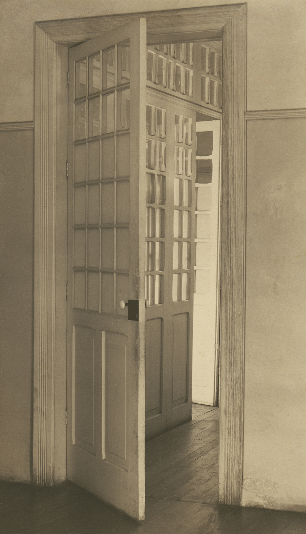 A photograph of a door ajar, with a light-filled room and another open door visible beyond it.