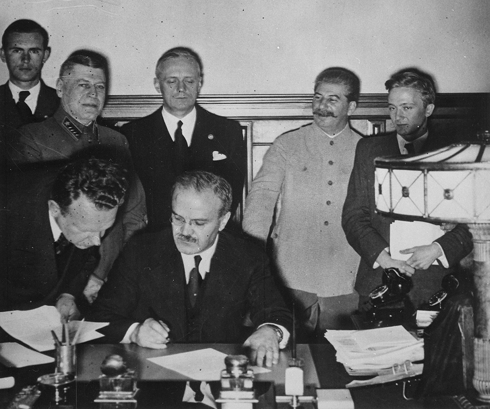 Soviet foreign minister Vyacheslav Molotov signs the German-Soviet Boundary and Friendship Treaty; Joachim von Ribbentrop and Joseph Stalin stand behind him, Moscow, September 28, 1939. U.S. National Archives and Records Administration.