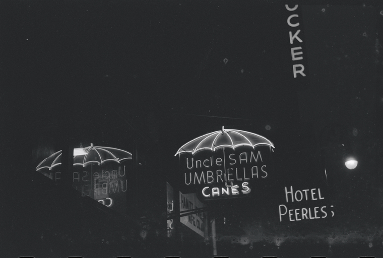 A black-and-white photograph of a neon sign shaped like an umbrella and the words uncle sam umbrellas canes.