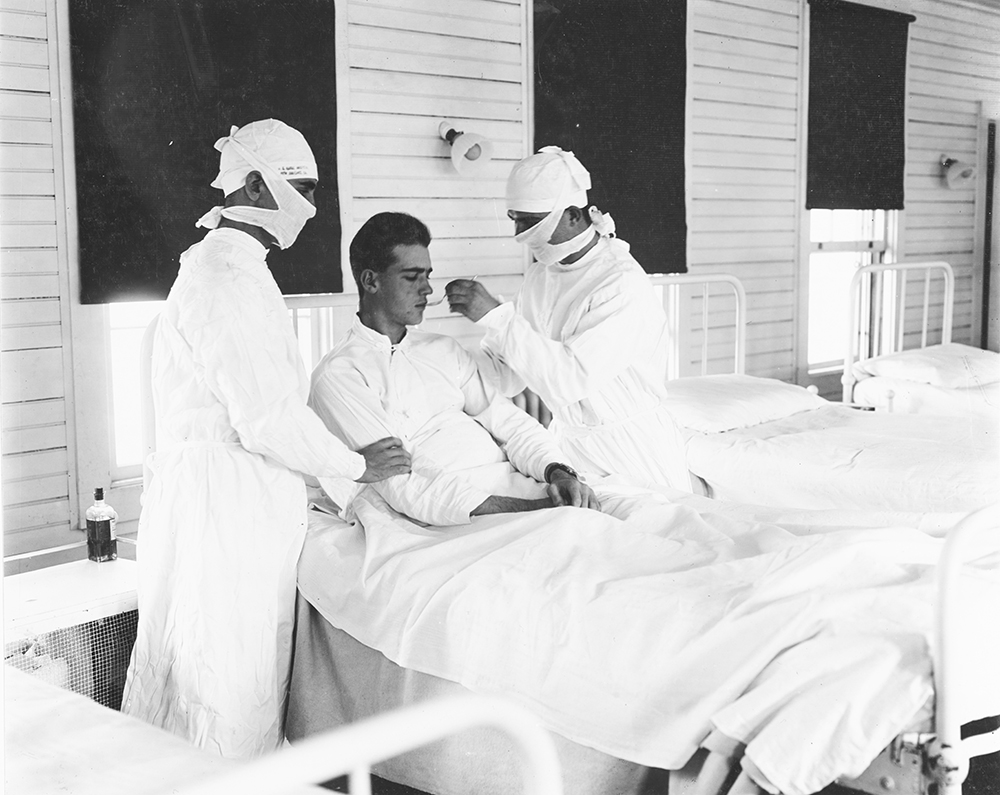 Masked medical personnel giving treatment to an influenza patient at a U.S. Naval Hospital, New Orleans, 1918. U.S. Naval History and Heritage Command.