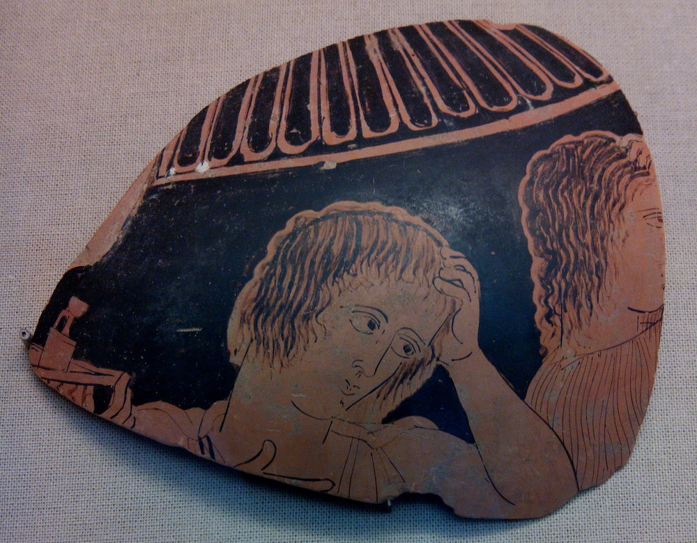 A piece of greek pottery showing a figure in mourning. The person is depicted with a hand on their heart, and holding their head in their other hand.