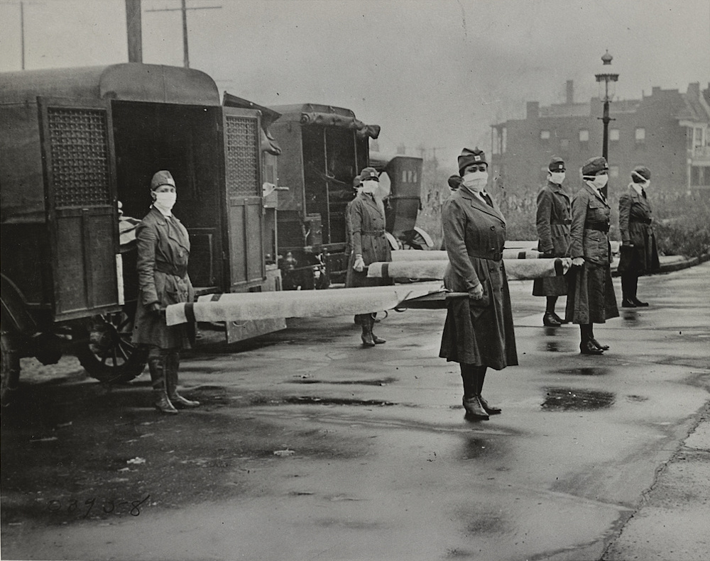 A photograph of Red Cross volunteers standing behind ambulances holding stretchers and wearing protective masks during the 1918 flu pandemic.