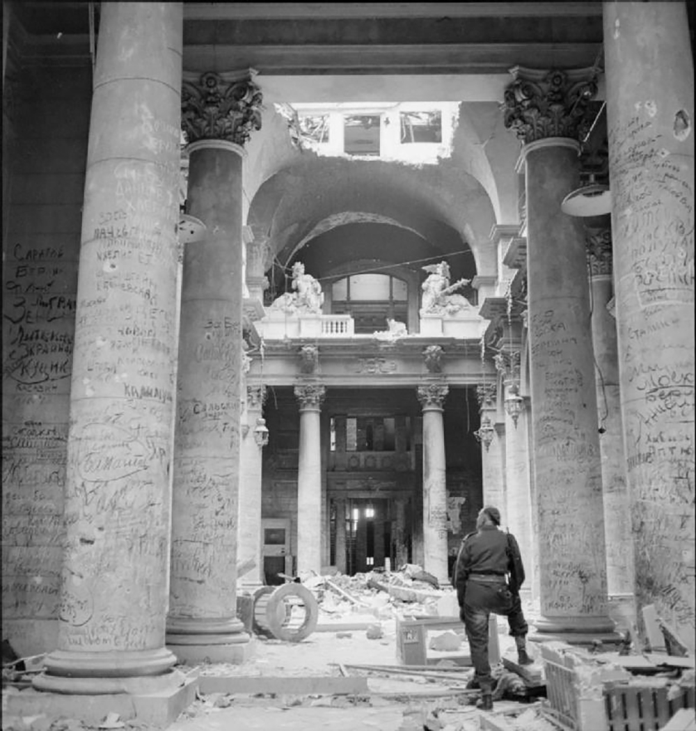 A British soldier stands among the ruins of the German Reichstag in Berlin, looking at pillars covered in graffiti left by Soviet soldiers, 1945. Wikimedia Commons, Imperial War Museums.