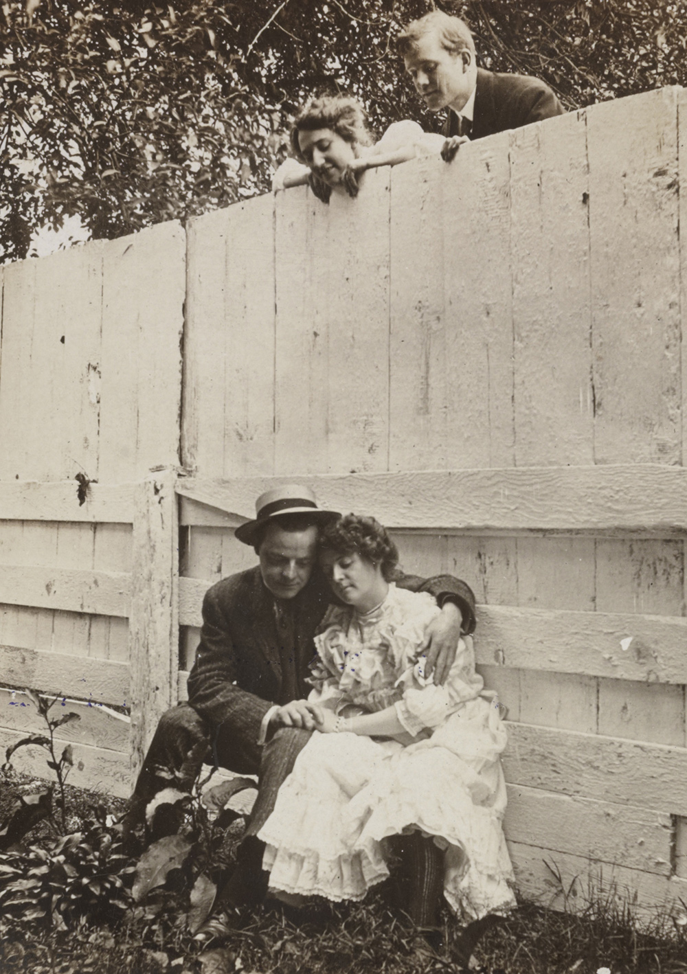Couple looking over fence at another couple.