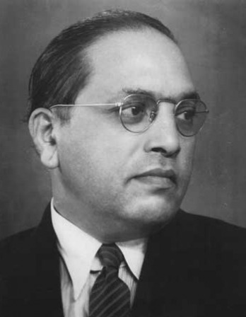 Profile of a man with wire-frame glasses and slicked-back hair looking right