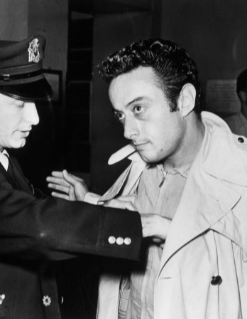 Black and white photo of Lenny Bruce being frisked by an officer