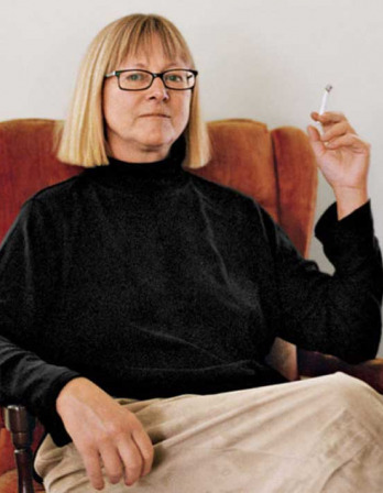 Seated woman wearing glasses and holding up a cigarette