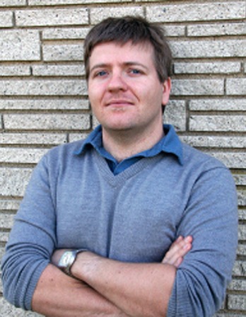 Photograph of Colin Dickey standing in front of a brick wall.