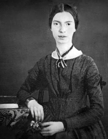 Black and white photograph of Emily Dickinson sitting next to a desk.