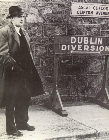 Flann O'Brien Flann O'Brien in an overcoat standing next to a Dublin Diversion sign