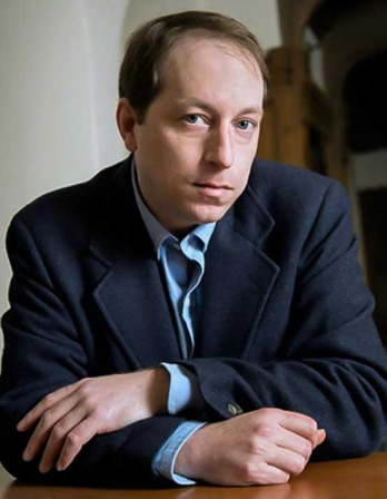 Man in a dark blue suit jacket seated at a desk