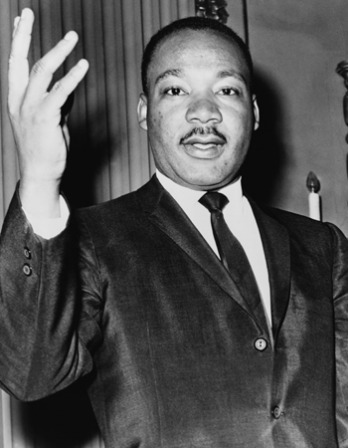 Black-and-white photograph of Martin Luther King Jr. with his right hand lifted
