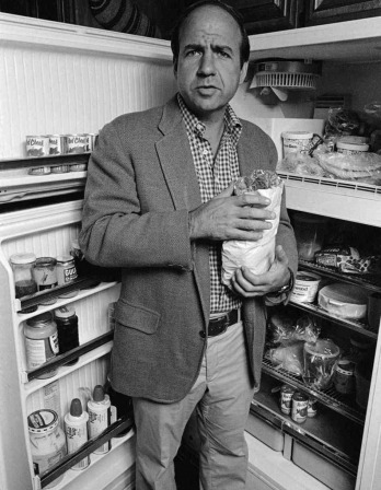 Calvin Trillin standing in front of a refrigerator in a black and white photograph
