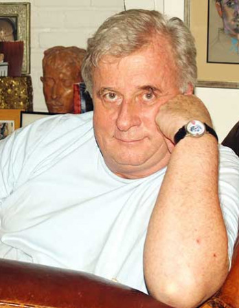 Photograph of a seated white-haired man in a white T-shirt