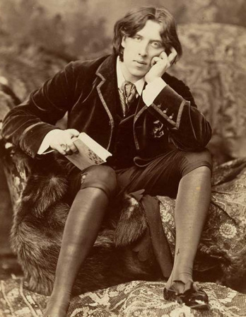 Sepia colored photo of Oscar Wilde sitting on a rock with a book in his hand