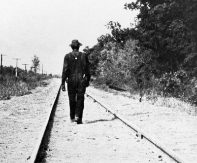 Hobo walking along railroad tracks, United States, c. 1930. Photographer unknown. © Private Collection / Peter Newark Pictures / Bridgeman Images.
