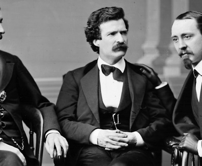 Black and white photograph of Mark Twain sitting between two men.