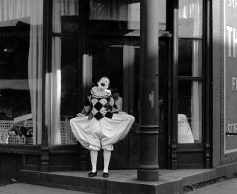 Black and white photograph of a clown laughing in front of a storefront.