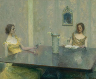 Two women wearing formal dresses sit at a large table, one reads a book. There is a vase of flowers at the center of the table.
