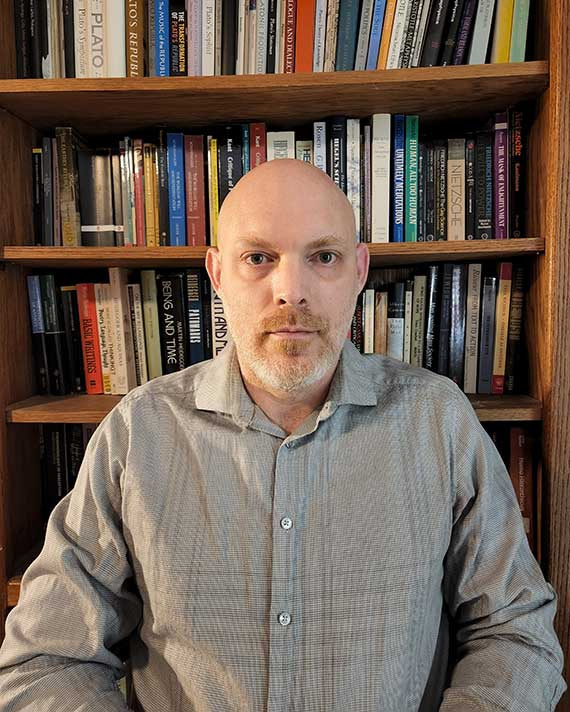 Man in gray shirt in front of bookshelf