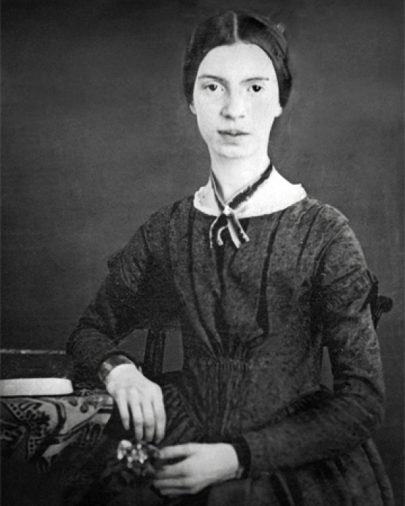 Black and white photograph of Emily Dickinson sitting next to a desk.