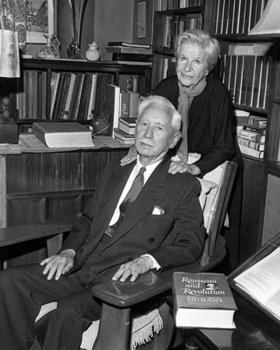 Seated man with a woman standing behind him with her hands on his shoulders.