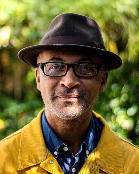 Man wearing a brown hat, black glasses, and a yellow corduroy jacket over a denim shirt