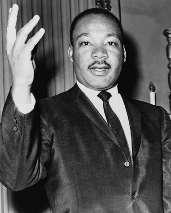 Black-and-white photograph of Martin Luther King Jr. with his right hand lifted