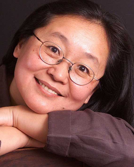 Aiping Mu Headshot of woman in glasses resting her head on her crossed arms