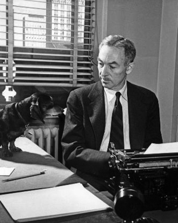 Black and white photograph of E. B. White sitting at his typewriter with his dachshund.
