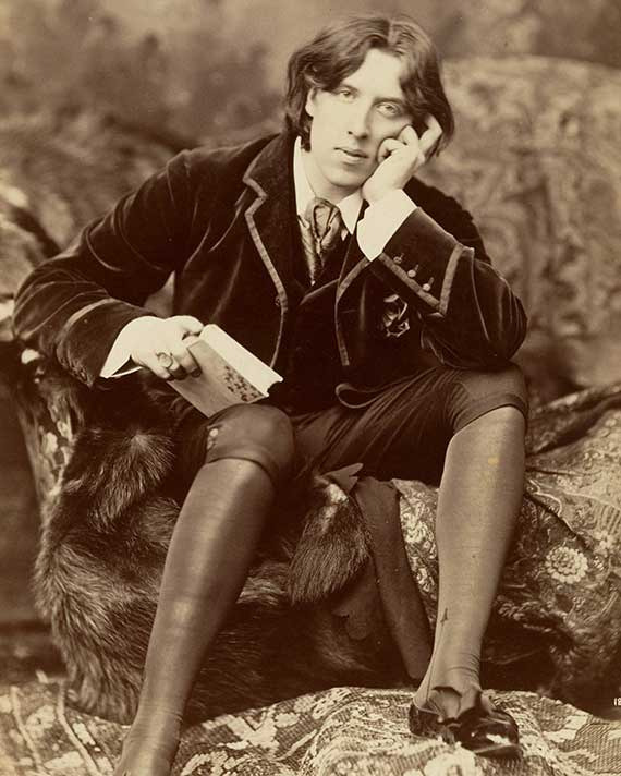 Sepia colored photo of Oscar Wilde sitting on a rock with a book in his hand
