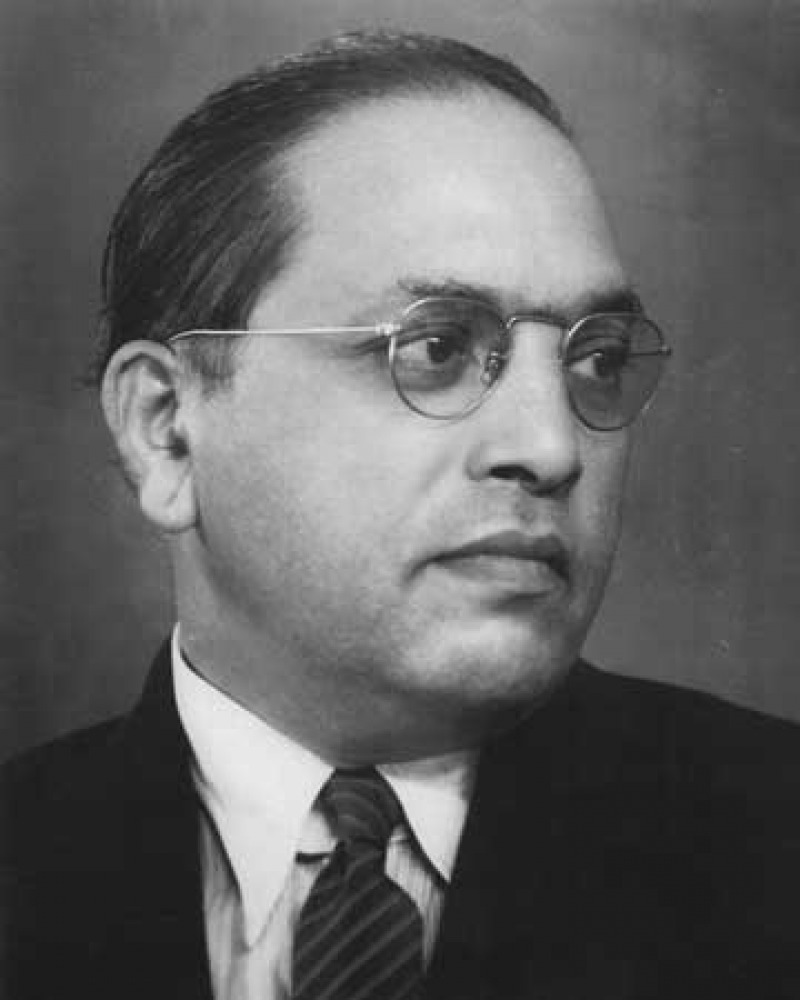 Profile of a man with wire-frame glasses and slicked-back hair looking right