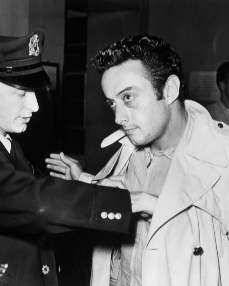 Black and white photo of Lenny Bruce being frisked by an officer