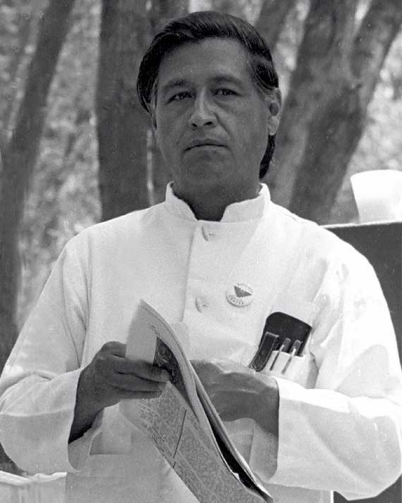 Black and white photograph of a dark-haired man in a white shirt holding a newspaper