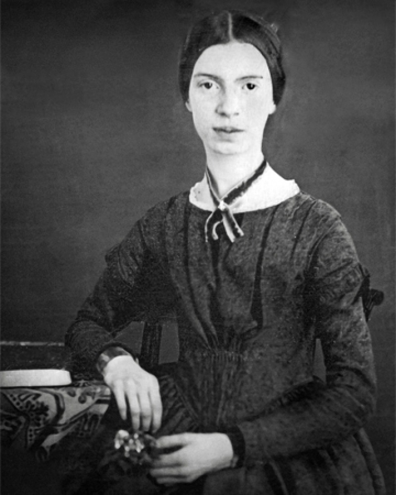 Black and white photograph of Emily Dickinson sitting next to a desk.