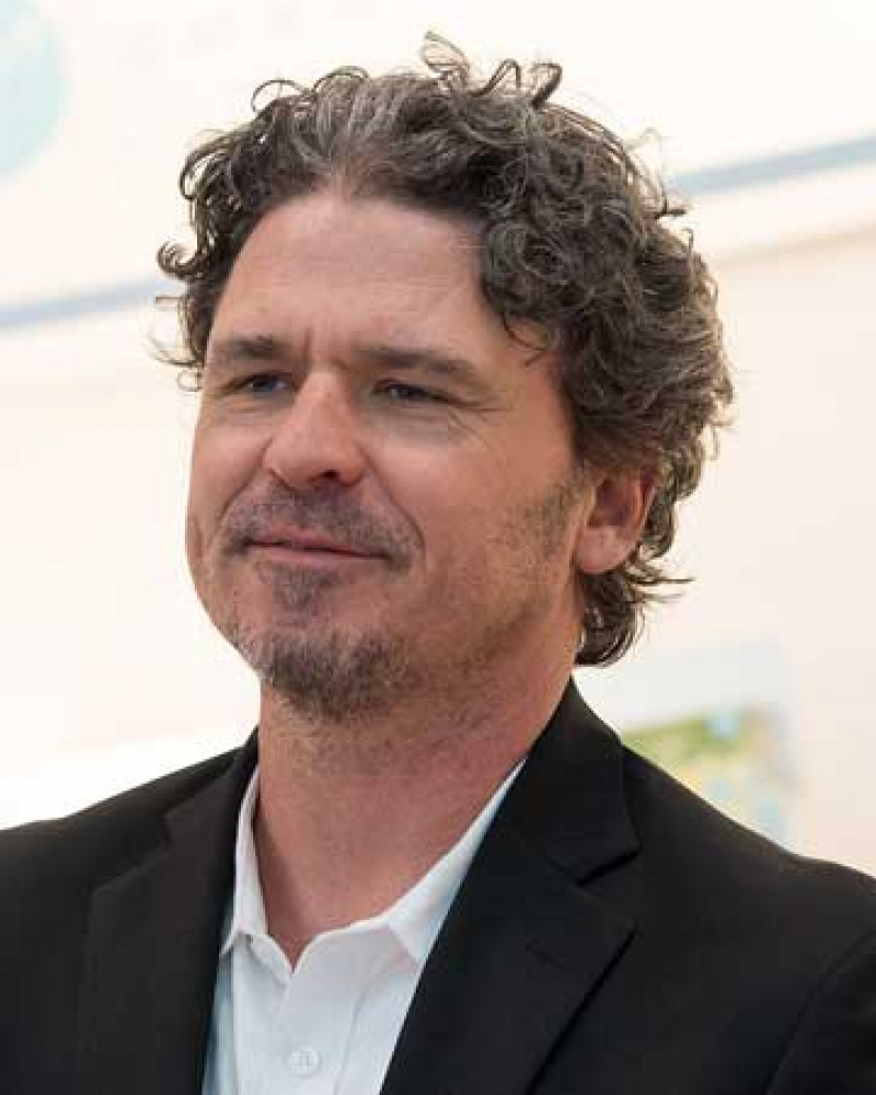 Profile of a man with curly hair and goatee wearing a black jacket and white shirt