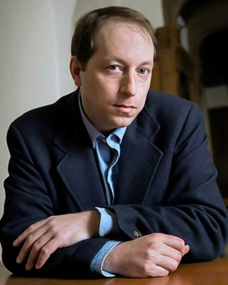Man in a dark blue suit jacket seated at a desk